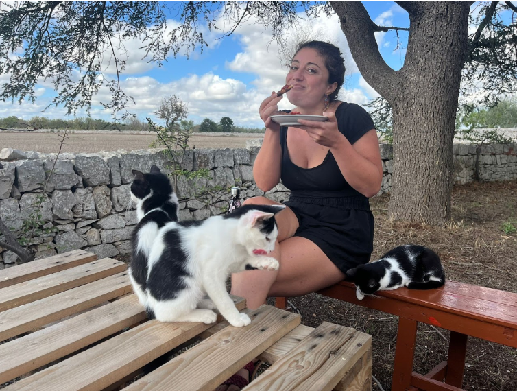 Digital nomad eating outdoors at Masseria Olga coliving in Italy, surrounded by friendly cats – rural coliving community experience