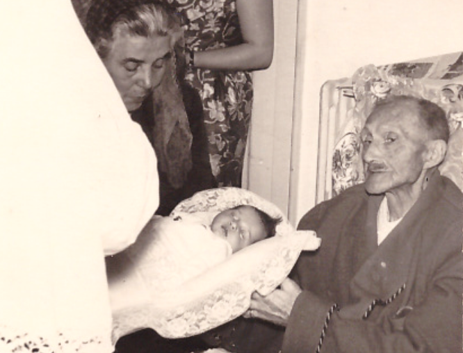 Elderly woman holding a newborn in a family gathering scene with multiple generations at Masseria Olga