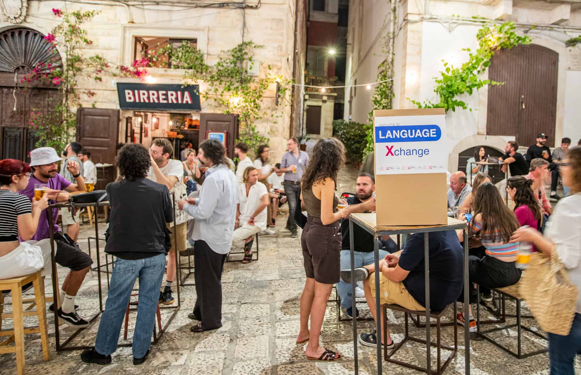 People chatting and enjoying drinks at a language exchange event in a charming Italian piazza in Puglia