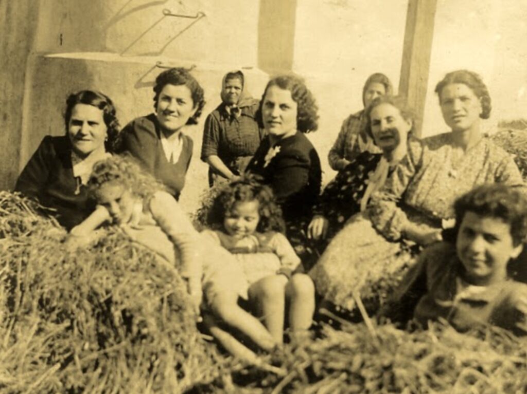 Vintage photo of women and children sitting on hay in front of the silo at Masseria Olga in the 1940s, including Olga and Anita