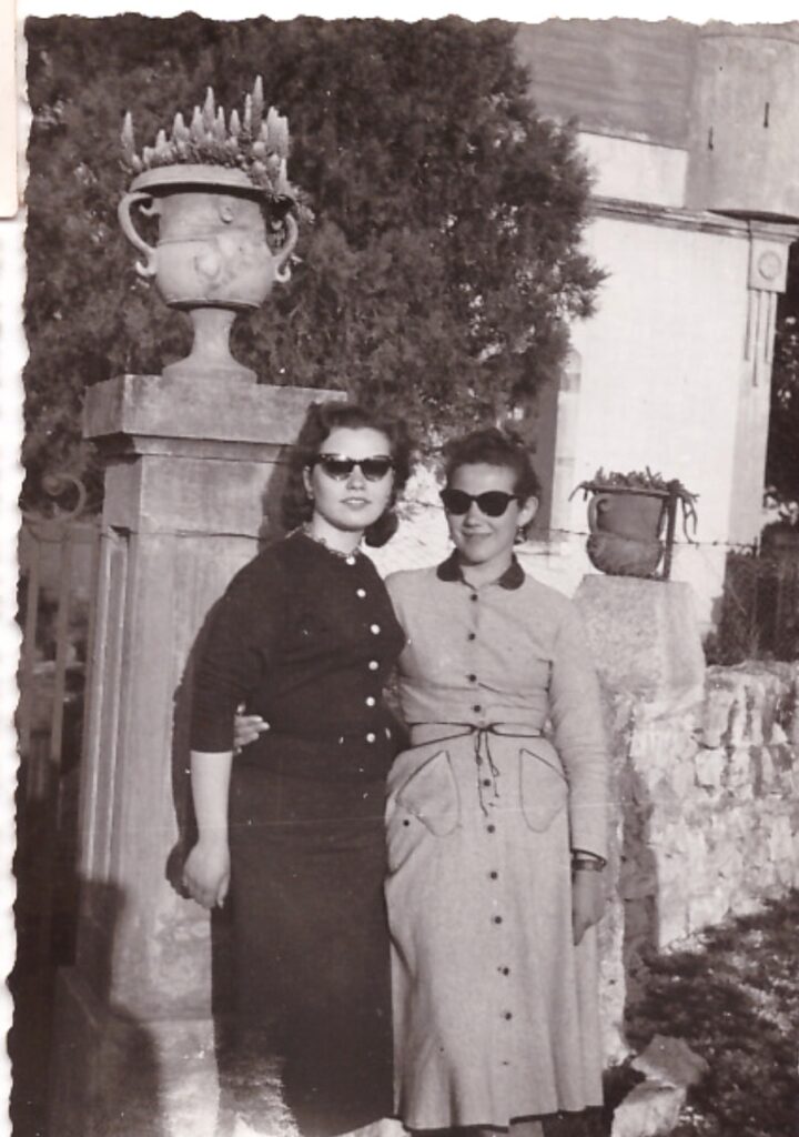 Olga on the right wearing a dress and sunglasses with her friend standing by a stone pillar in front of Masseria Olga in Puglia