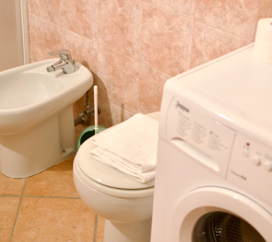 Toilet, bidet and washing machine in the shared bathroom used by the single room guests at Masseria Olga coliving in Italy.