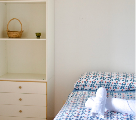 Neatly prepared single bed with fresh towel and open shelves in a single room at Masseria Olga coliving in Italy.