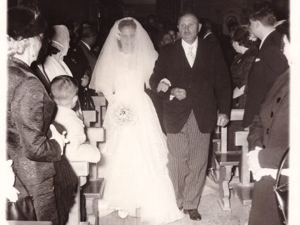 Black and white photo of a bride walking down the aisle with her father during a wedding ceremony surrounded by guests in church